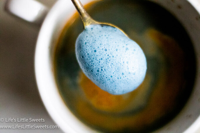 a spoonful of frothy blue milk foam over a mug of espresso