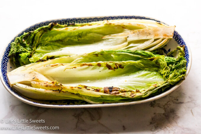 a horizontal photo of cooked, grilled green, Napa Cabbage on an oval platter plate over a white marble surface