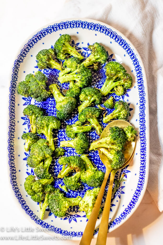 an oval plate with cooked broccoli and 2 gold serving spoons