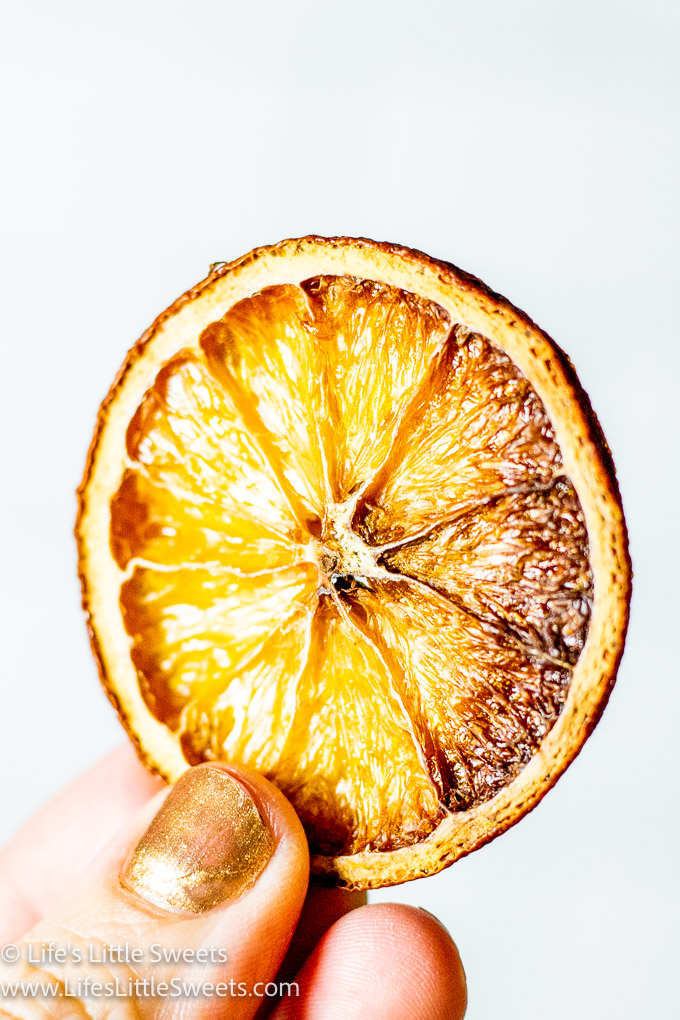 a dried orange slice being held by a hand with a white background