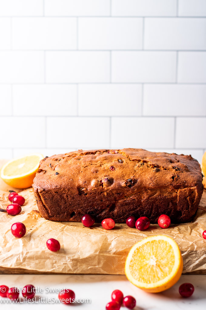 a loaf of bread on parchment paper with cranberries and oranges