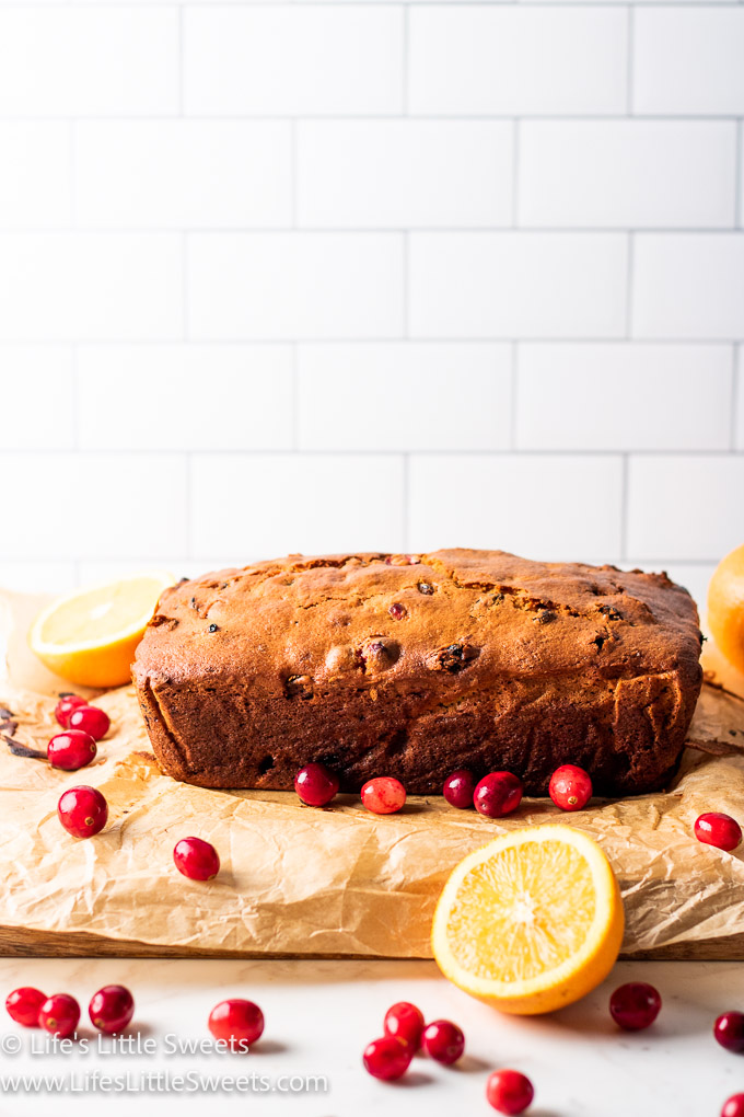 a loaf of quickbread with oranges and cranberries with a white subway tile background