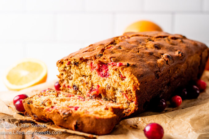 a loaf of cranberry bread with the end cut off on parchment paper with oranges and cranberries around it