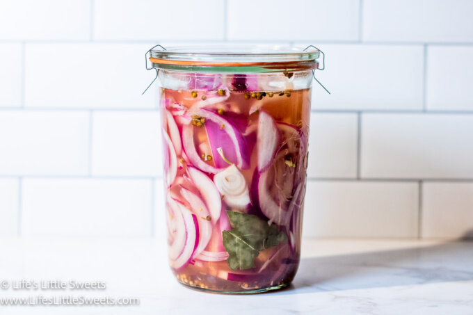 pickled red onions in a jar on a white kitchen counter with white subway tile in the background