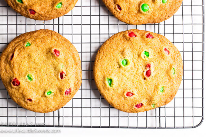 Several Christmas M&M cookies on a wire cooling rack on a white surface