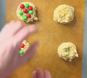 a hand placing M&Ms on top of cookie dough balls before baking