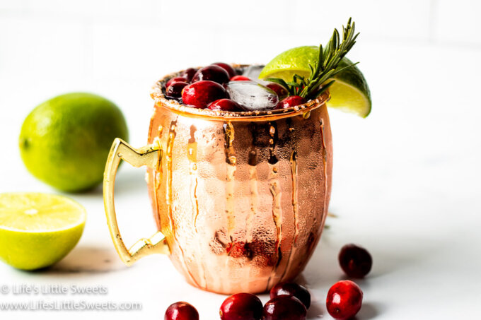 a cold drink with cranberries, a lime wedge and a sprig of rosemary