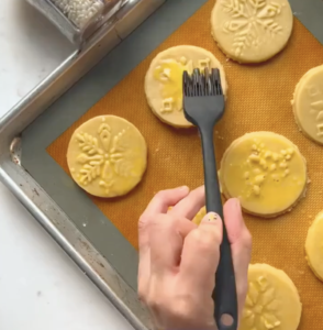 applying egg wash to a sugar cookie