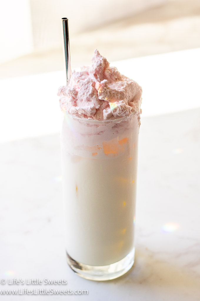 milk with ice in a tall glass with pink whipped cream on top