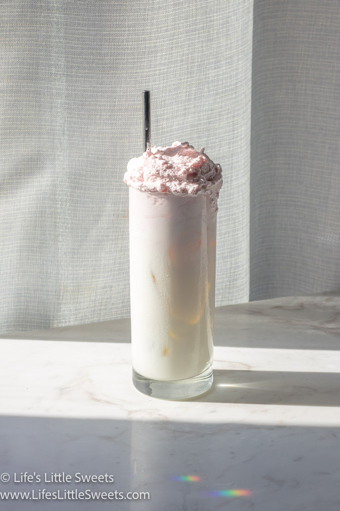 a sunny photo of pink whipped cream over icy cold milk in a tall glass with a metal straw