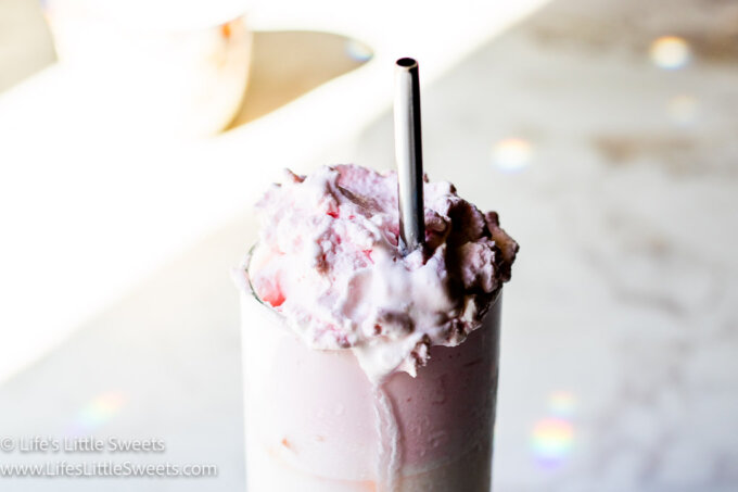 a horizontal photo of whipped strawberry milk with a metal straw
