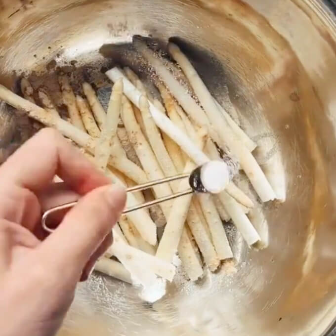 adding seasonings to fresh asparagus in a metal bowl