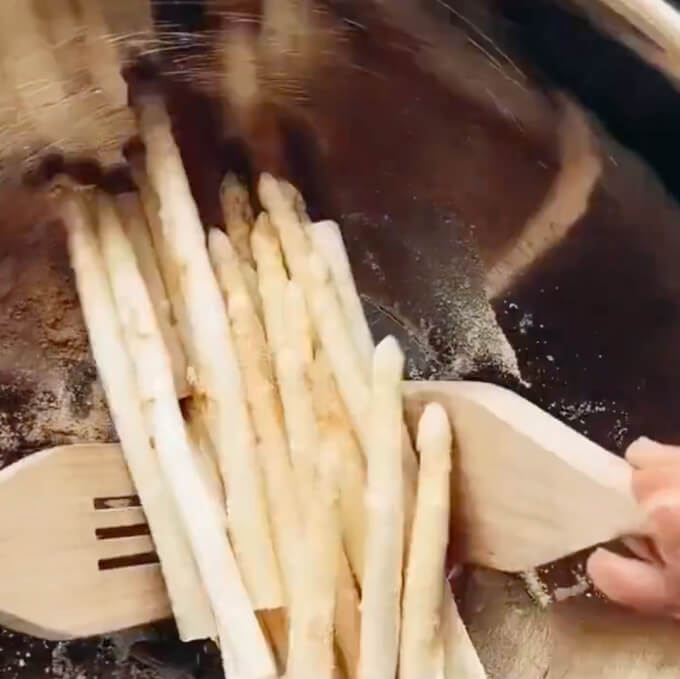 wooden utensils tossing fresh asparagus with seasonings in a metal bowl