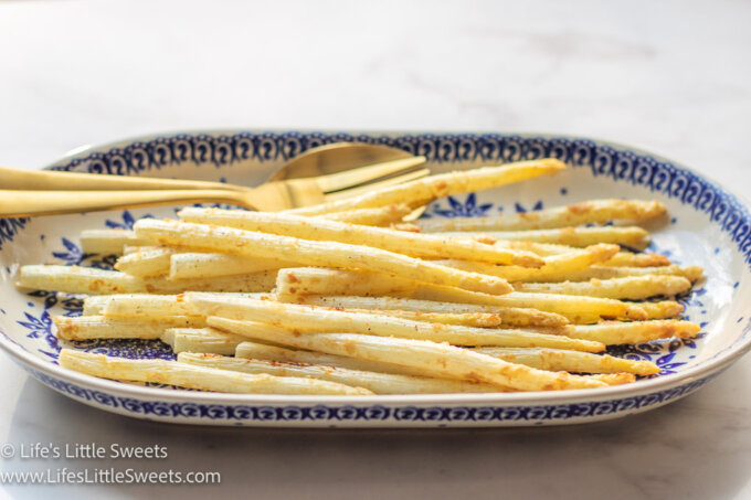 cooked white asparagus with gold utensils on an oval plate on a marble table