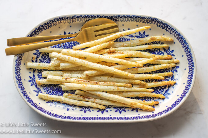 overhead view of white asparagus on an oval plate with gold utensils