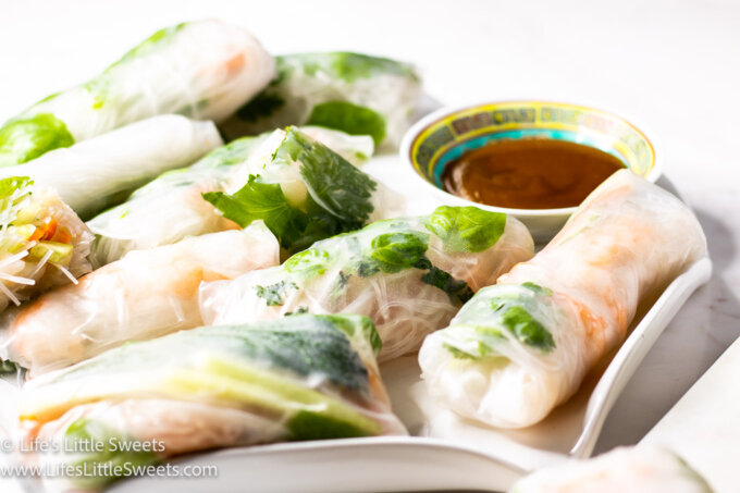 a photo of several fresh spring rolls with a brown sauce on a white surface