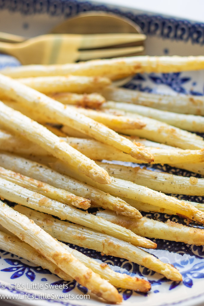 a close up view of cooked white asparagus on a blue and white patterned plate with gold utensils