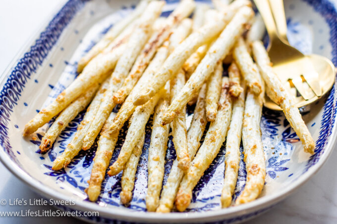 an angled view of cooked white asparagus on an oval plate with gold utensils