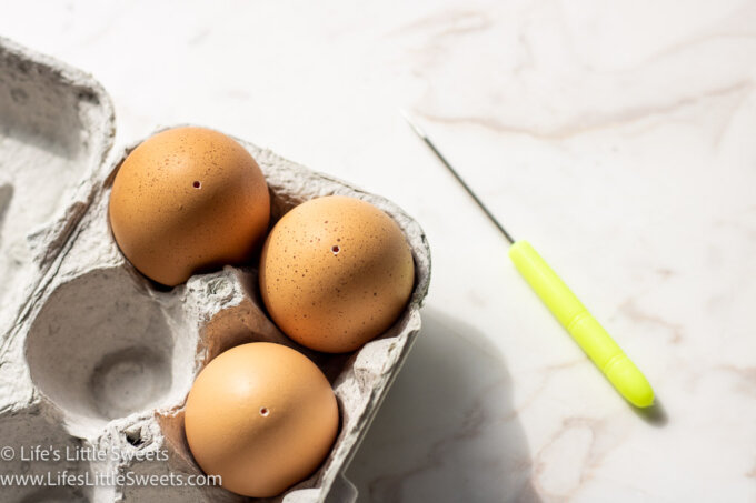 blown out eggs in a carton with a felting needle in the background on a white marble table surface