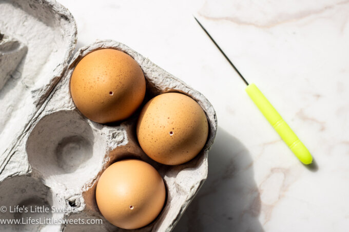 blown out eggs in a carton with a felting needle in the background on a white marble surface