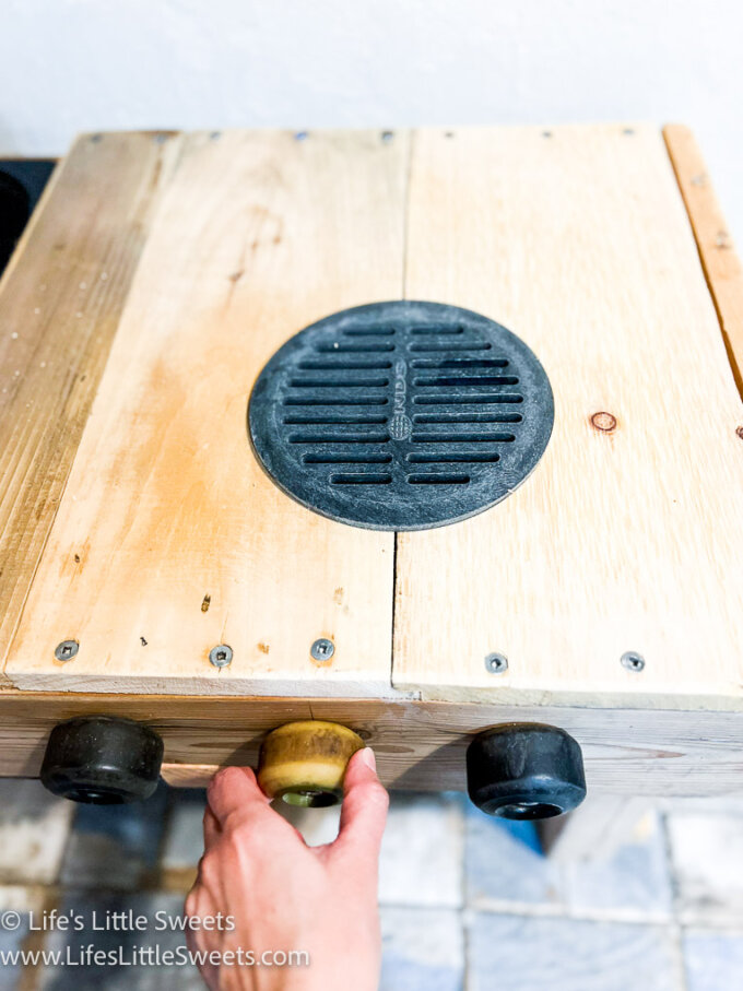 a hand turning the knob of a wood mud kitchen