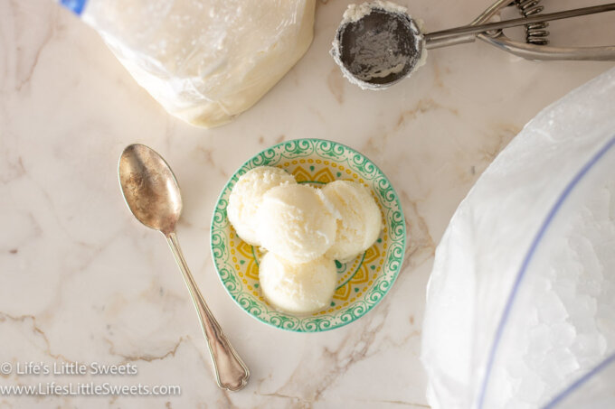 many scoops of plain vanilla ice cream made in a double bag in a shallow colorful dish on a white marble surface with a silver spoon