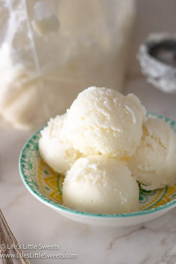 several scoops of plain vanilla ice cream in a shallow colorful dish on a white marble surface with a silver spoon