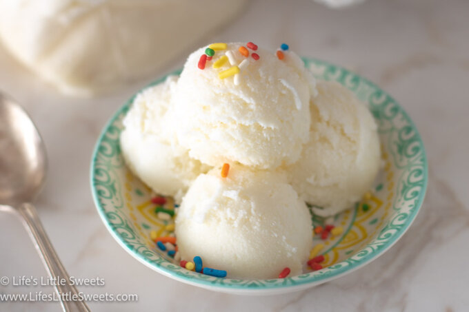 scoops of plain vanilla ice cream (with sprinkles) in a shallow colorful dish on a white marble surface with a silver spoon