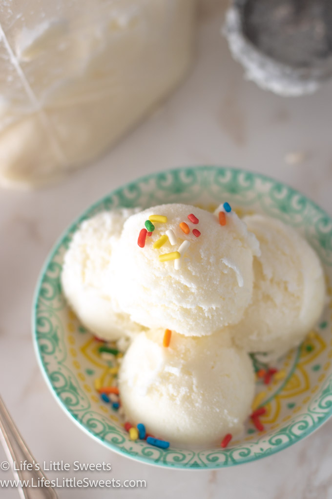 scoops of vanilla ice cream with sprinkles in a shallow colorful dish on a white marble surface with a silver spoon