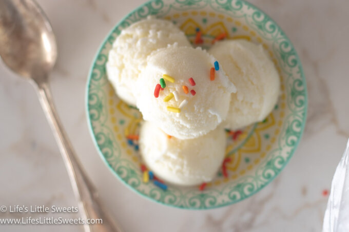 scoops of plain vanilla ice cream (with colorful sprinkles) in a shallow colorful dish on a white marble surface with a silver spoon