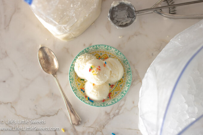 scoops of plain vanilla ice cream in a shallow colorful dish on a white marble surface with a silver spoon and a scoop