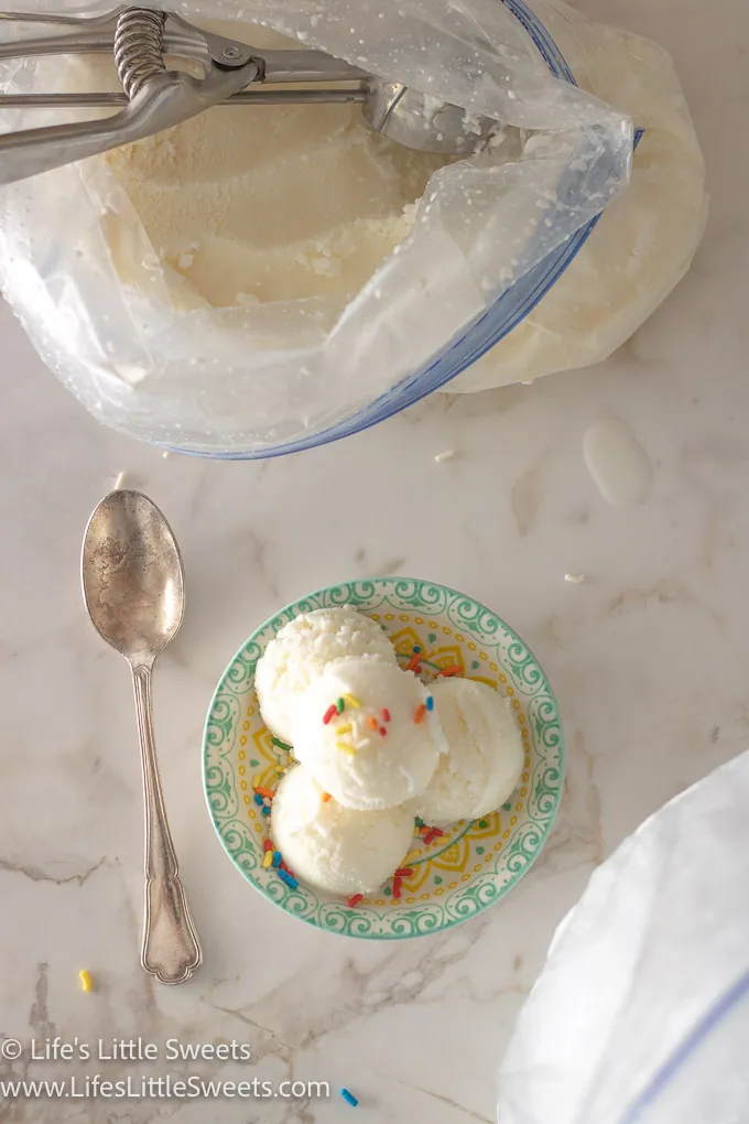 scoops of homemade vanilla ice cream with sprinkles in a shallow colorful dish on a white marble surface with a silver spoon