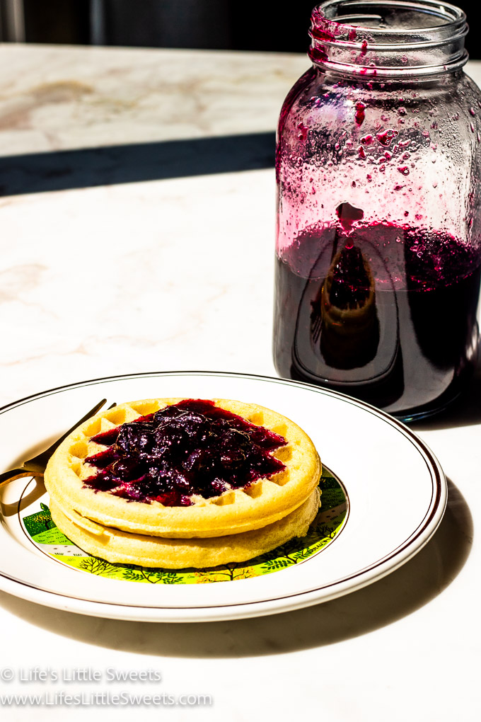 blueberry syrup on waffles and in a jar on a marble surface
