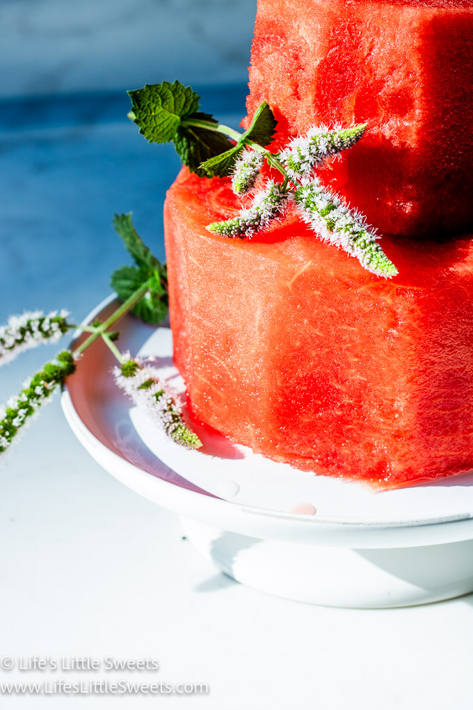 a watermelon cake on a white cake stand with fresh, flowering mint