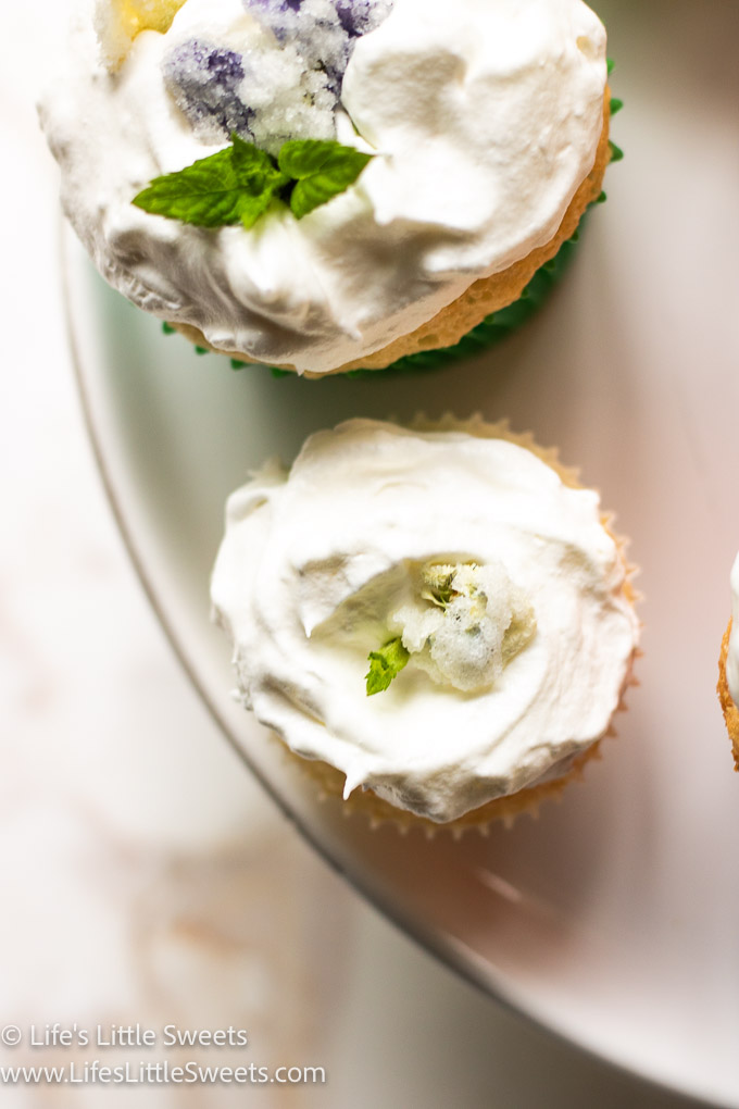 light-colored, angel food cupcakes decorated with white frosting and mint leaves and sugared violets
