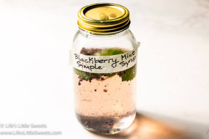 a jar of blackberry mint simple syrup (labeled) with a lid on top on a white surface