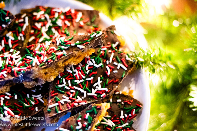 a white plate filled with Christmas Chocolate Toffee near a white-lighted Christmas tree