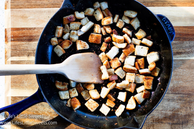 croutons in a cast iron skilled with a wooden spatula