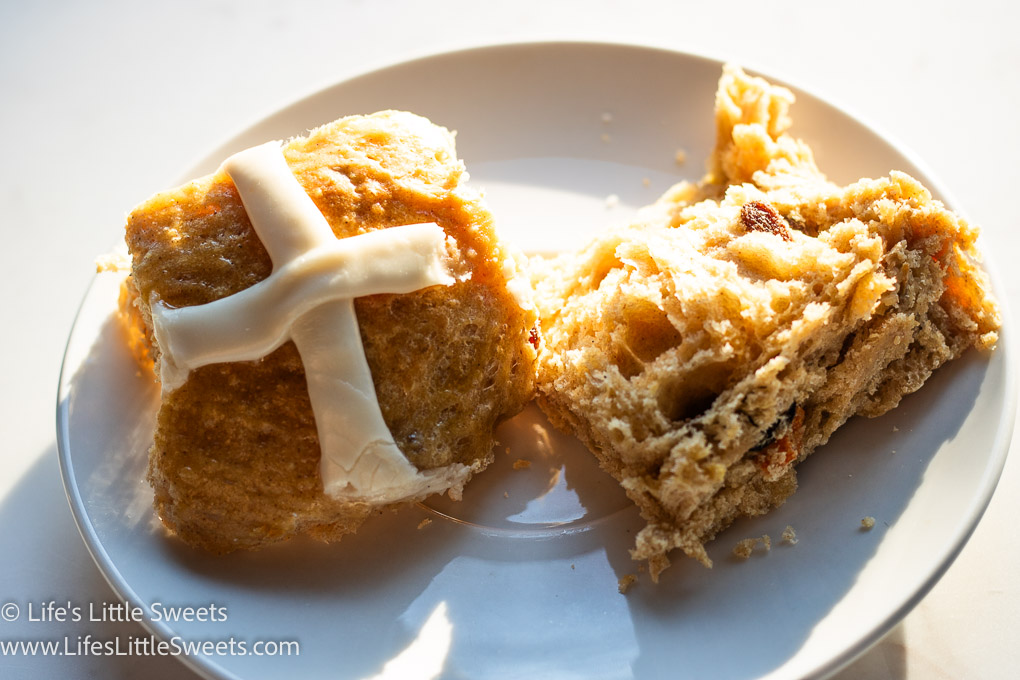 a hot cross bun on a white plate in the sunlight on a marble table